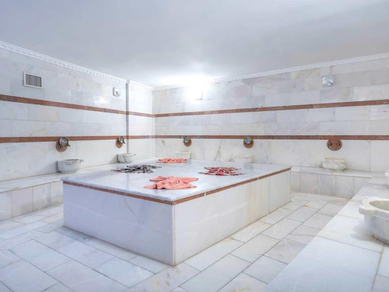 Intérieur d'un hammam lumineux avec un large marbre central et des murs carrelés blancs.