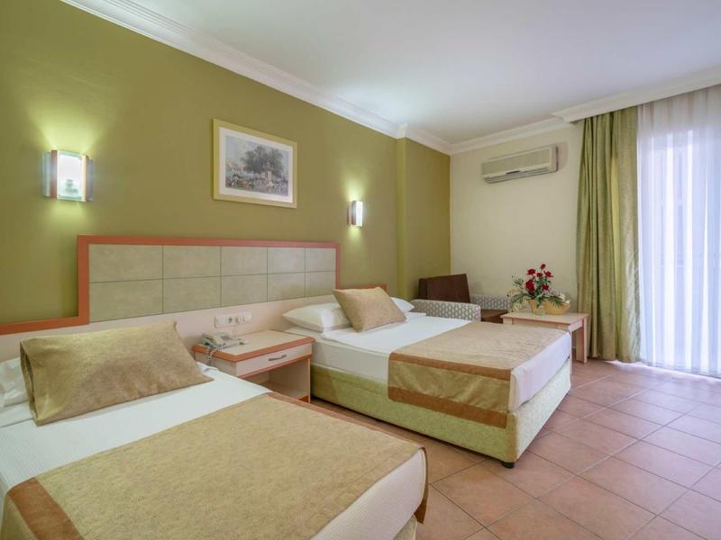 Chambre d'hôtel moderne avec deux lits simples, lumière douce et grande fenêtre voilée.