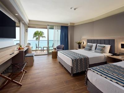 Moderní hotelový pokoj s výhledem na moře, manželskou a jednolůžkovou postelí, dřevěnou podlahou a balkonem.