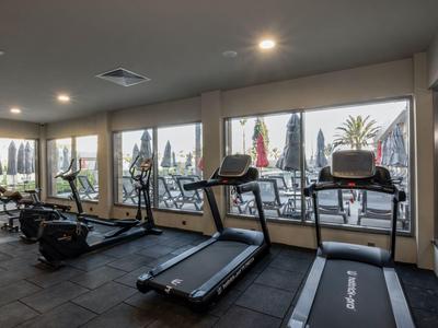 Fitnessraum mit Laufbändern und Ausblick auf den Poolbereich im Hotel.