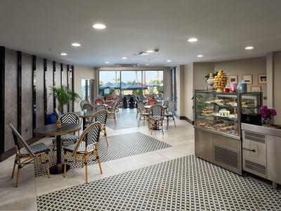 Moderní kavárna s stolky, židlemi a vitrínou na pečivo.