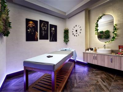 Moderně zařízená wellness místnost s masážním stolem, rostlinami a dekorativními obrazy na stěně.