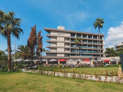 Modernes Hotelgebäude mit mehreren Stockwerken, umgeben von Palmen und Sonnenschirmen auf einer Rasenfläche.