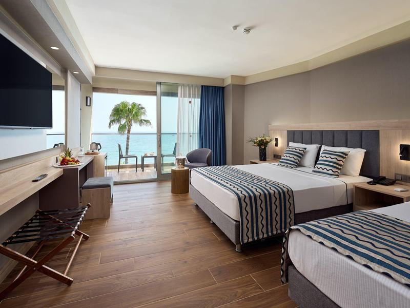 Moderní hotelový pokoj s výhledem na moře, manželskou a jednolůžkovou postelí, dřevěnou podlahou a balkonem.