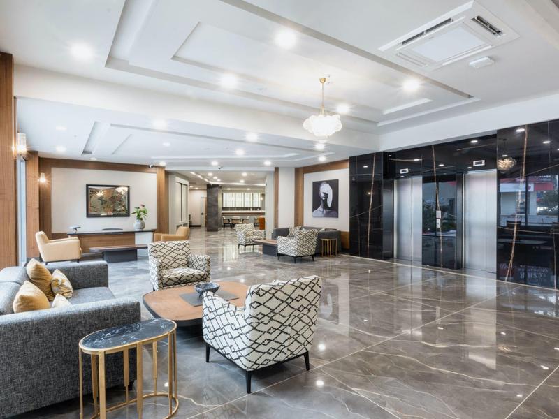 Světlá a moderní hotelová lobby s posezením, mramorovou podlahou a výtahy.