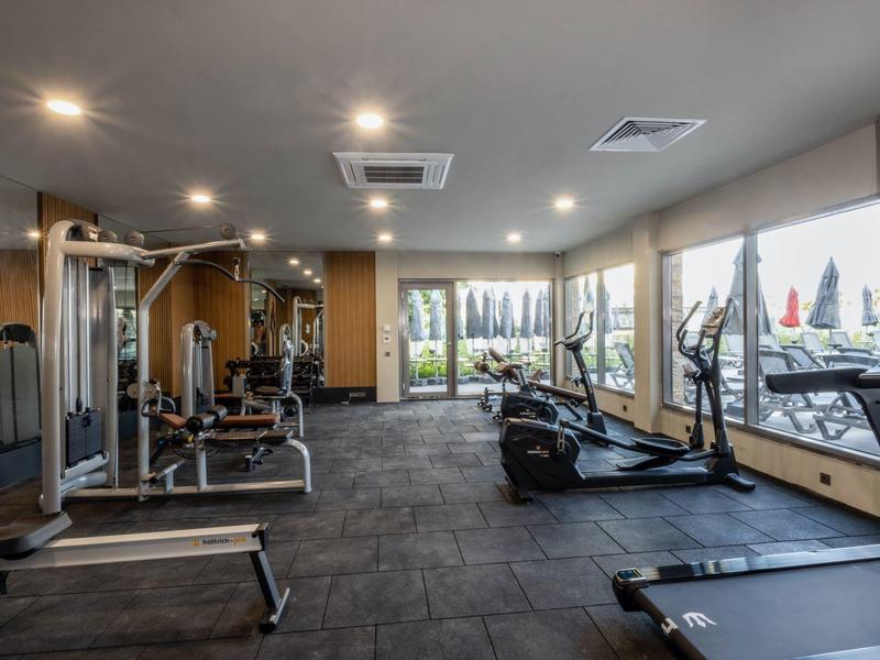 Moderní posilovna s různými tréninkovými stroji a velkými okny s výhledem ven.