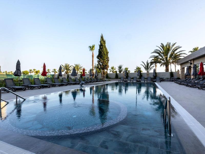 Moderní hotelový bazén s lehátky a palmami pod jasnou oblohou.