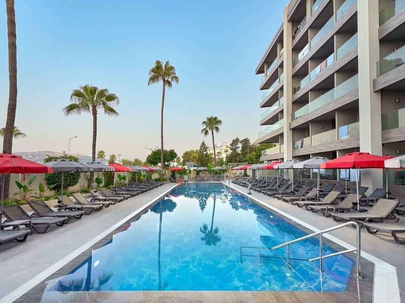 Moderní hotelový bazén s lehátky a červenými slunečníky vedle vícepatrové budovy.