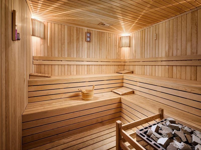 Pohodlná sauna s dřevěnými lavicemi, osvětlením a saunovou kamny s kameny.