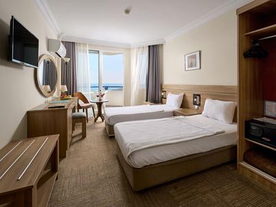 Camera d'hotel con due letti singoli, scrivania, TV e vista sul mare.