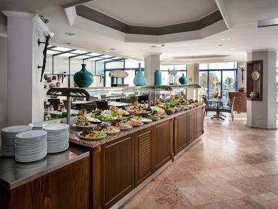 Buffet con piatti vari e tavoli apparecchiati in una luminosa sala ristorante dell'hotel.