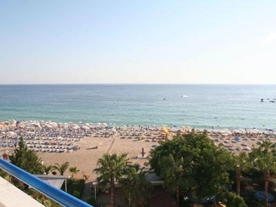 Uitzicht vanaf het balkon op een druk zandstrand met parasols en palmbomen aan zee.