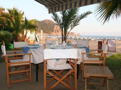 Terrasgedeelte met gedekte tafels en houten stoelen op een strand met een berg op de achtergrond