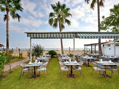 Außenbereich eines Strandrestaurants mit gedeckten Tischen und Palmen bei bewölktem Himmel