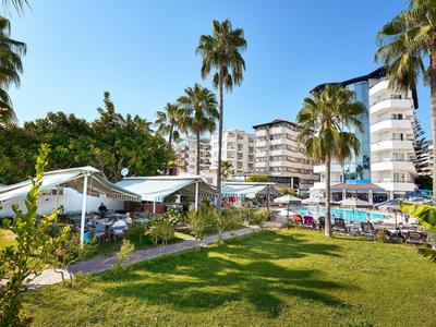 Hotelgebäude mit Balkonen, umgeben von Palmen und grüner Rasenfläche unter blauem Himmel.