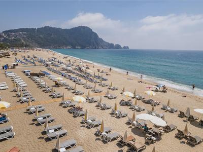 Lunga spiaggia sabbiosa con file di lettini e ombrelloni vicino a montagne e mare.