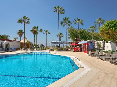Grande piscina blu con palme e lettini in un giardino di un hotel soleggiato.
