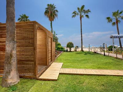 Bungalow moderno in legno con palme e prato curato sotto un cielo blu.