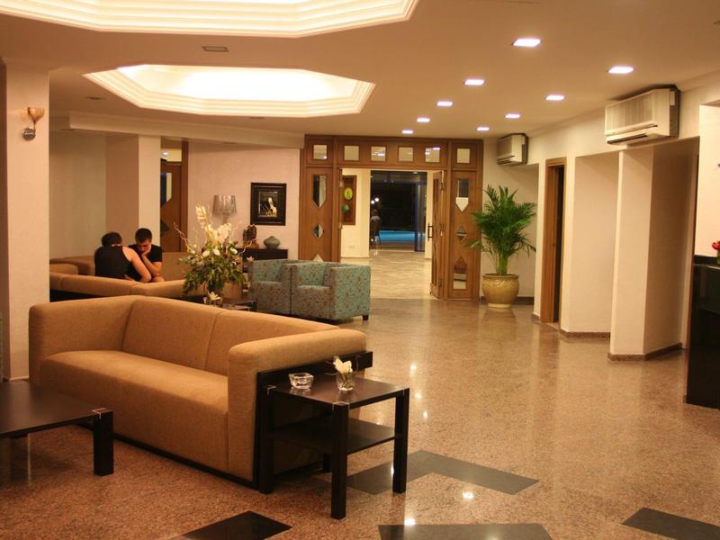 Hel verlichte hotel lobby met zithoeken, planten en receptie op de achtergrond.