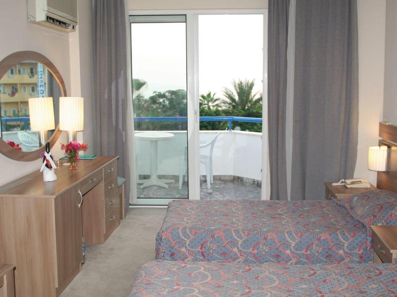 Hotelkamer met twee bedden, dressoir, ronde spiegel en balkon met zeezicht.