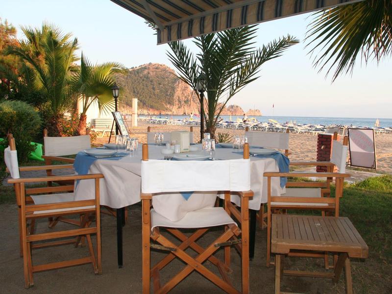 Terras met gedekte tafel en stoelen bij het strand met palmbomen en heuvel op de achtergrond.