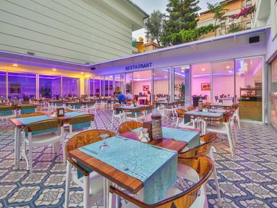 Zweistöckiges Café mit blau beleuchteter Terrasse, Holztischen und Stühlen auf gemustertem Boden.