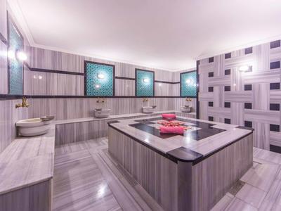 Modernes Badezimmer mit großer Badewanne, grauen Fliesen und drei beleuchteten Bildern.