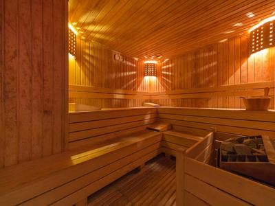 Holzsauna mit mehrstufigen Sitzbänken, warmem Licht und Saunaofen in der Ecke.