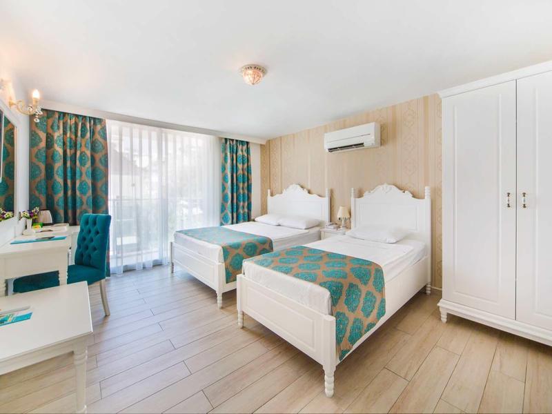 Helles Hotelzimmer mit zwei Einzelbetten, Schreibtisch, Schrank und großem Fenster mit Vorhängen.