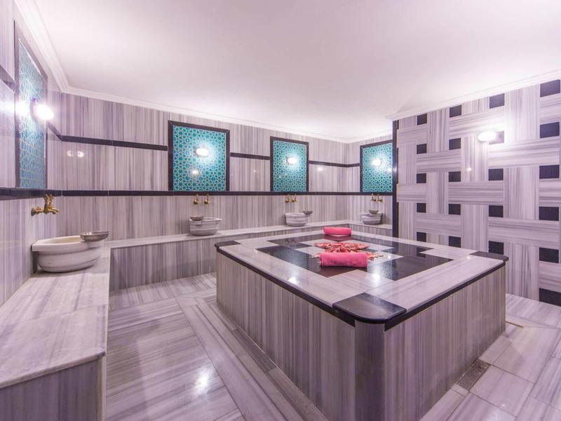 Modernes Badezimmer mit großer Badewanne, grauen Fliesen und drei beleuchteten Bildern.