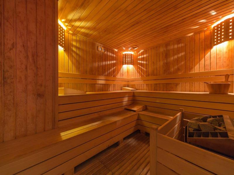 Holzsauna mit mehrstufigen Sitzbänken, warmem Licht und Saunaofen in der Ecke.