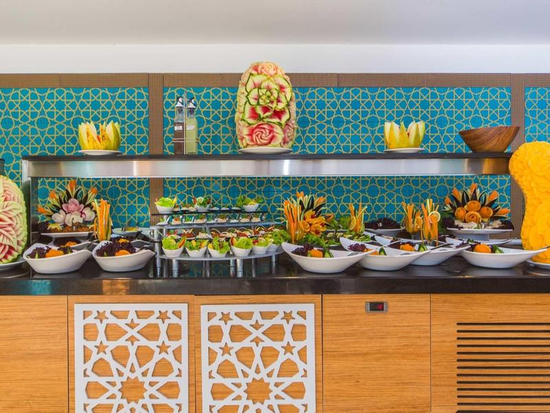 Buffet mit kunstvoll geschnitztem Obst und Gemüse vor blau gemusterter Wand.