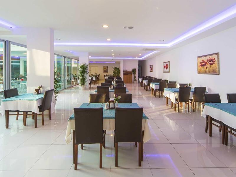 Heller, moderner Speisesaal mit vielen Tischen und schwarzen Stühlen, Glasfront und Fliesenboden.