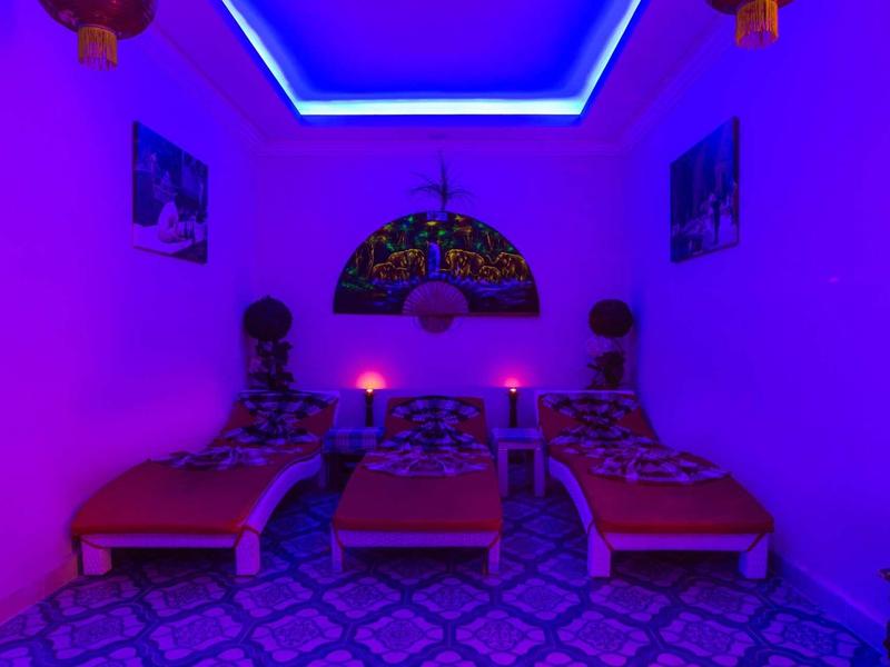 Drei Betten in einem Raum mit blau-lila LED-Beleuchtung und gemustertem Boden.