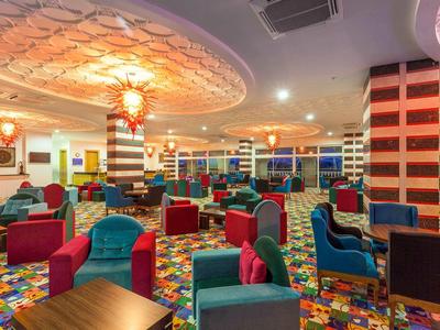 Bunte Cocktailbar mit roten und blauen Sesseln und gemustertem Teppichboden unter heller Deckenbeleuchtung.