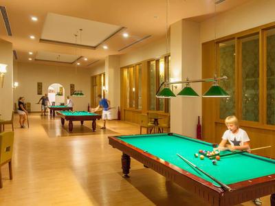 Bambini che giocano a biliardo in una spaziosa stanza ben illuminata con pavimenti in legno e grandi finestre.