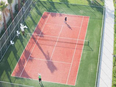 Vista aerea di un campo da tennis con due giocatori e spettatori accanto alla recinzione.