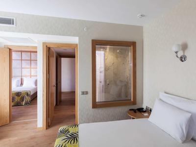 Helles Schlafzimmer mit weißem Bett, Holztüren, großem Spiegel und modernem Wandschirm.