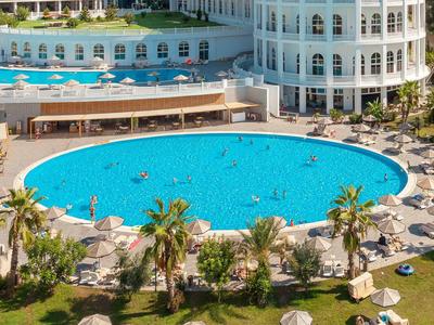 Grande piscina rotonda davanti a un hotel bianco con lettini e piante