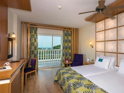 Helles Hotelzimmer mit Doppelbett, Balkon, Leseecke, Schreibtisch und Blick auf das Meer.