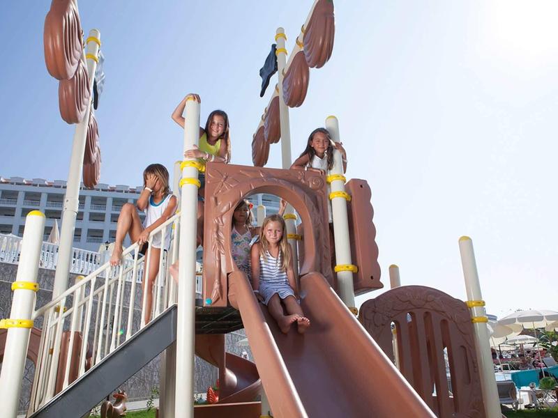 Kinder spielen auf einem braunen Spielplatz-Rutschbahn bei sonnigem Wetter im Freien.