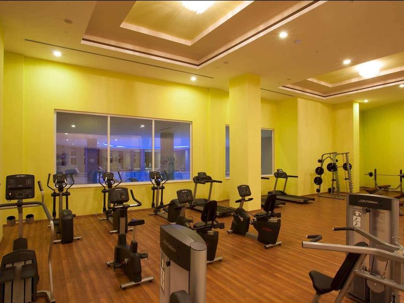 Ein heller Fitnessraum mit verschiedenen Trainingsgeräten auf Holzfußboden und gelben Wänden.