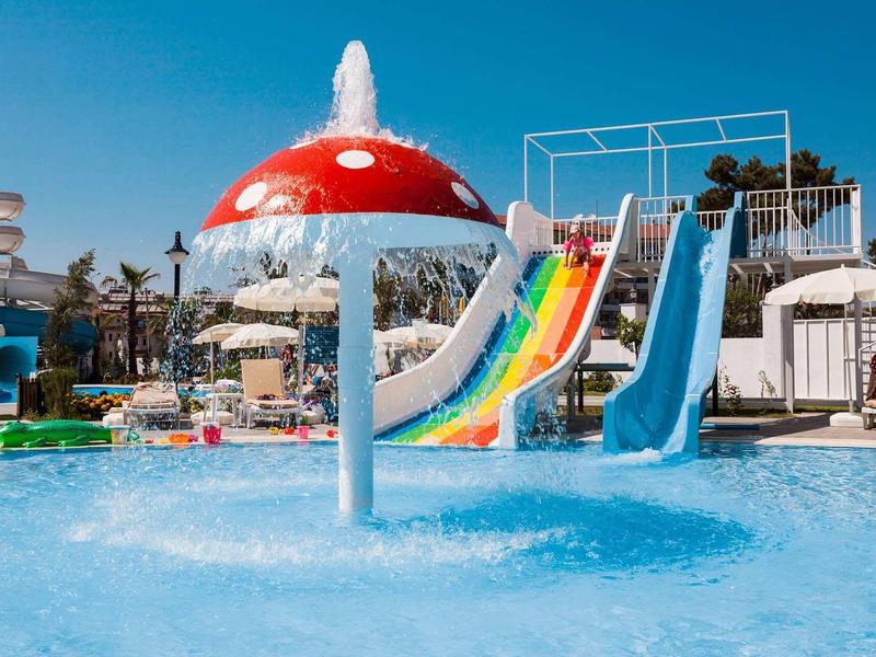 Bunter Wasserrutschenpark mit Pilz-Sprudler und klarem blauem Himmel im Hintergrund.