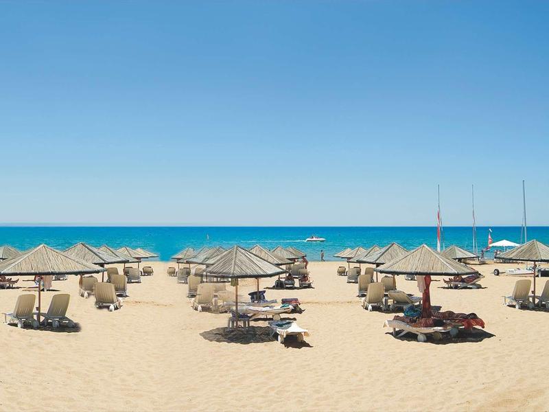 Strand mit Sonnenschirmen, Liegen und blauem Himmel, ruhiges Meer im Hintergrund.