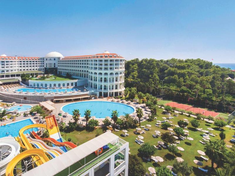 Großes Hotel mit mehreren Pools, Wasserrutschen, Liegestühlen und Grünflächen neben einem Wald und Meer.