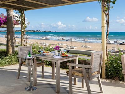 Nastavený stůl na terase s výhledem na moře a písečnou pláž v pozadí.