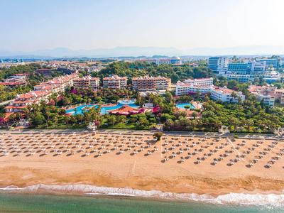 Letecký pohled na hotel s velkým bazénem vedle dlouhé písečné pláže s plážovými slunečníky u moře.