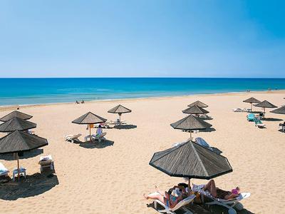 Široká písečná pláž s deštníky a hosty pod modrou oblohou u moře.