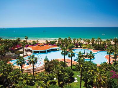Vista di una piscina dell'hotel con palme e mare sullo sfondo sotto un cielo sereno.