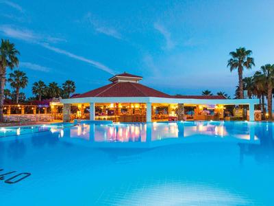 Piscina illuminata con area lounge e palme al tramonto in un resort.
